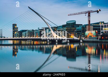 Samuel Becket bridge at sunset, lights reflecting off the River Liffey.Office buildings in Dublin financial district at nigh. Golden hour cityscape. Stock Photo