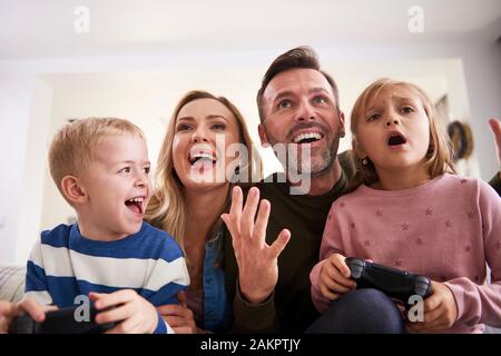 Emotional parents and children playing video game at home Stock Photo