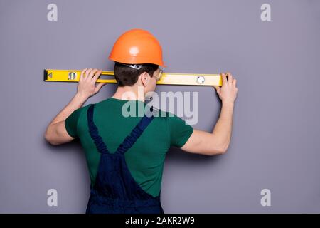 Rear behind view photo of handsome masculine worker guy skilled engineer measure rack length of wall wear t-shirt safety dungarees protective helmet Stock Photo