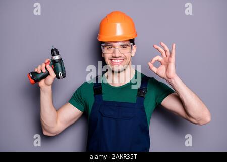 Photo of handsome masculine worker guy skilled engineer hold electric drill showing okey symbol wear t-shirt safety dungarees protective helmet Stock Photo