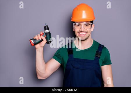 Portrait of confident cool man repairer hold perforator ready to renew flat apartment wear blue overalls green t-shirt isolated over grey color Stock Photo