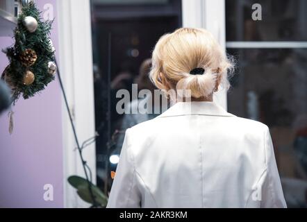 The woman is standing with her back to the camera and you can see her reflection in the window. Stock Photo