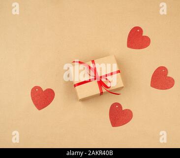 gift wrapped in brown kraft paper and tied with a thin silk ribbon on a background of paper, top view. Congratulations on Valentine's Day February 14 Stock Photo