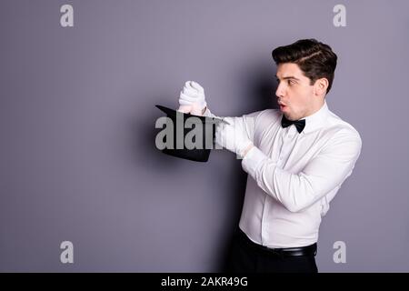 Profile side photo of funky wizard magician impressed by miracle making focus hold hare ears he pull out of cylinder hat wear white shirt black bow Stock Photo