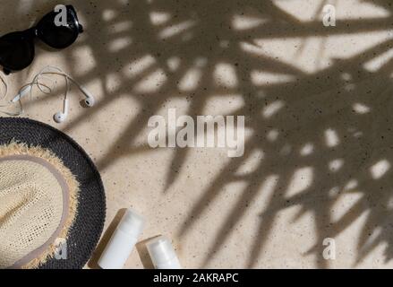 Summer composition contain hat, sunglasses, sunscreen and headphones with palm leaf shadows Stock Photo