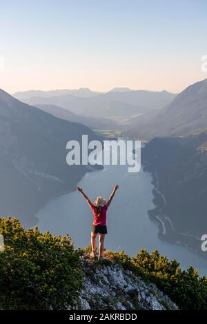 Young woman stretches arms in the air, view from the mountain Baerenkopf to Lake Achensee, Tyrol, Austria Stock Photo