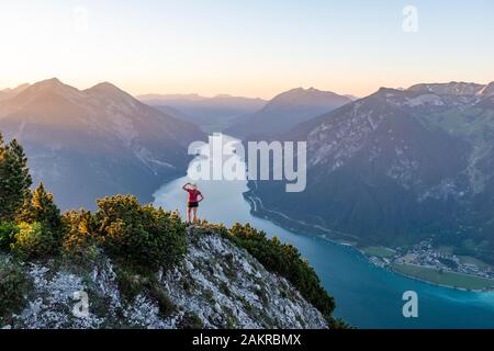 Sunset, young woman looking over mountain landscape, view from the mountain Baerenkopf to Lake Achensee, left Seebergspitze and Seekarspitze, right Stock Photo