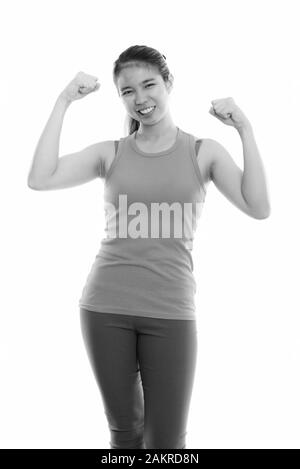 Studio shot of young happy Asian woman smiling while flexing both arms ready for gym Stock Photo