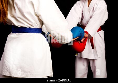 Two little karate women in white kimonos, one in red and the other in blue competition equipment shake hands as a sign of respect before the fight aga Stock Photo