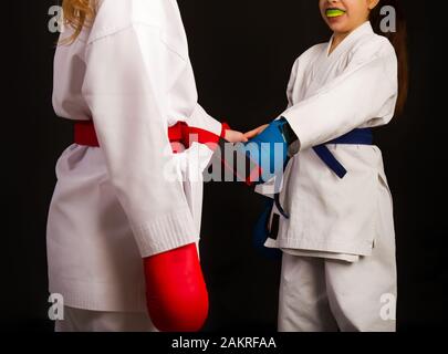 Two little karate women in white kimonos, one in red and the other in blue competition equipment shake hands as a sign of respect before the fight aga Stock Photo