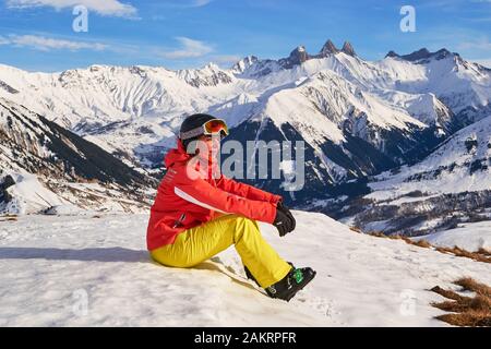 Skier woman taking a break above Saint-Jean-d'Arves village, France, in Les Sybelles ski resort, admiring the sunset. Winter activities. Stock Photo