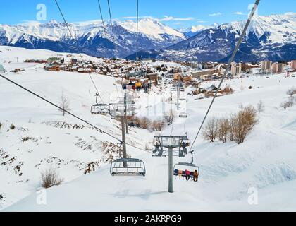 Les Sybelles, France - March 12, 2019: View from a ski chair lift moving up the mountain, in the Winter, above La Toussuire mountain village, part of Stock Photo