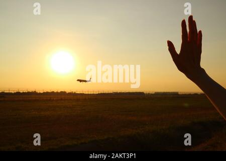 Silhouette of woman's hand waving to the airplane against sunset sky Stock Photo