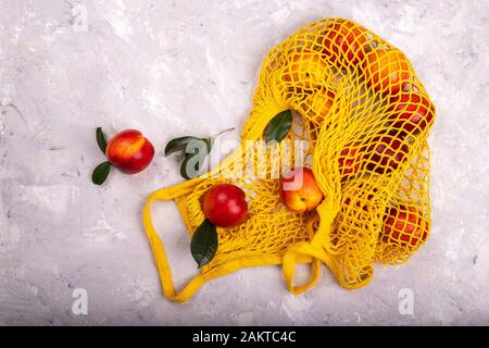 Nectarines in yellow string mesh reusable bag on the table Stock Photo