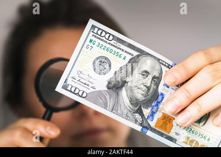 A man checks the authenticity of a hundred-dollar bill. Concept on the topic of fake money Stock Photo