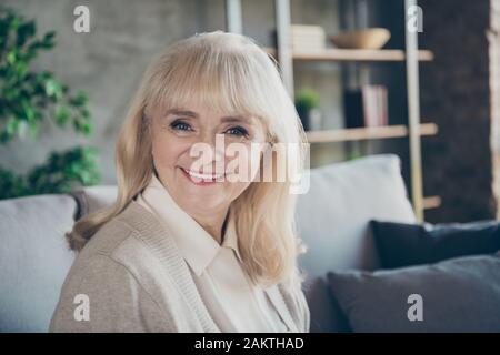 Closeup photo of amazing blond adorable aged granny homey good mood toothy beaming smiling cheerful sitting comfort sofa divan living room indoors Stock Photo