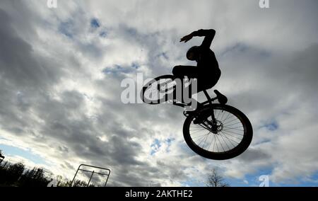 10 January 2020, Hessen, Frankfurt/Main: A teenager jumps with his dirtjump bike on the skater area in the Osthafenpark in front of a cloudy sky. Photo: Arne Dedert/dpa Stock Photo