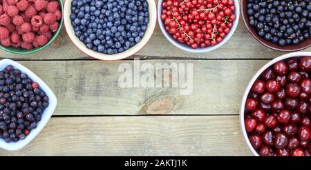 Many bowls with fresh garden and forest berries: raspberry, blueberry, red and black currant, sweet cherries overhead on the wooden table, flat lay, f Stock Photo