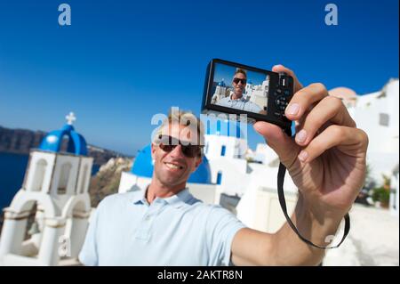 Smiling tourist taking a self portrait photo in Santorini, Greece under bright blue Mediterranean sky Stock Photo