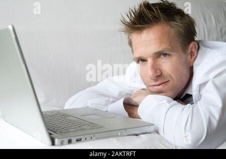 Man in smart casual unbuttoned white shirt lying on white sofa with his laptop computer Stock Photo