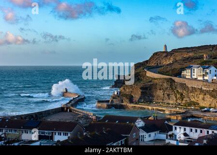 Stormy weather at Portreath, Cornwall, UK with waves breaking over the Monkey Hut and the Pepperpot visible on the high cliff. Stock Photo
