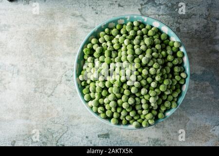 high angle view of a pile of frozen green peas in a light blue ceramic bowl, on a table Stock Photo