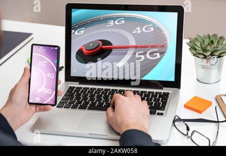 5G, internet speed test, high speed concept. Man holding a mobile phone, speedometer 5G speed network connection on the computer laptop screen, busine Stock Photo