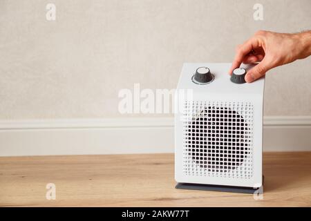 Man's hand adjusts the temperature of the electric fan heater at home in winter time. White domestic electric heater on floor indoor Stock Photo