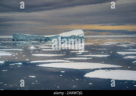 Picturesque view of big iceberg floating among the ice in cold waters of Antarctica, under heavy grey cloudy sky Stock Photo