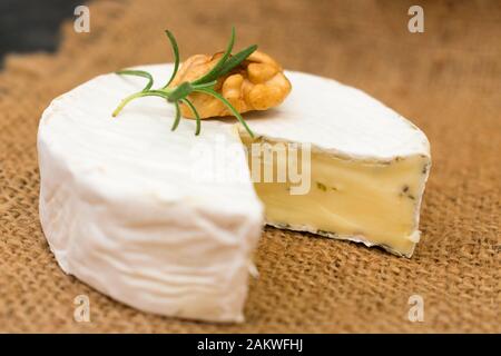 Camembert cheese with herbs, decorated with a sprig of rosemary and walnut. Close-up. Stock Photo
