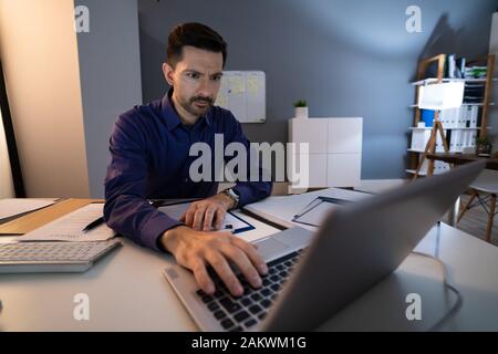 Mid Adult Businessman Working Late At Desk In Office Stock Photo