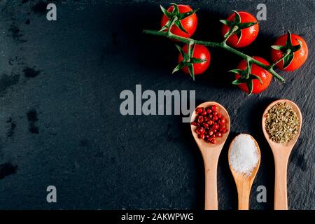 top view background of colorful food ingredients :  fresh cherry tomatoes, spices tablespoons. healthy mediterranean  diet. Dark background Stock Photo
