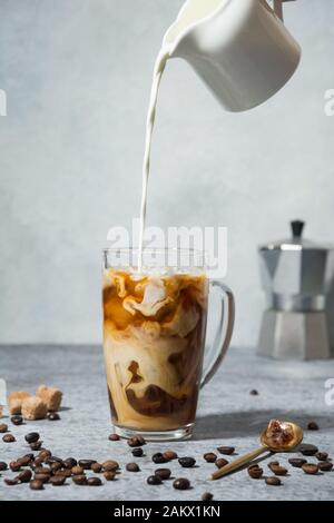 Iced latte coffee in cup glass with pouring milk on grey Stock Photo