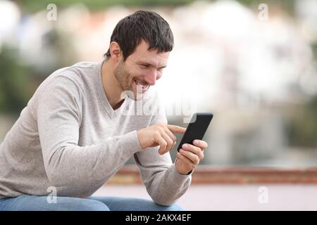 Happy man sitting on a bench using mobile phone in a rural town Stock Photo