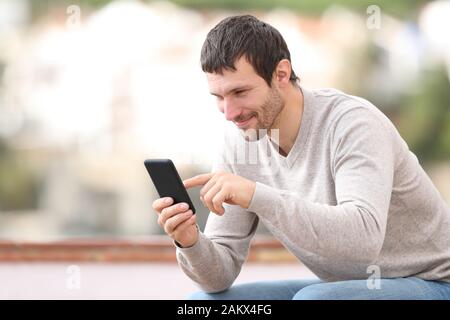 Satisfied man sitting on a bench using mobile phone in a town Stock Photo