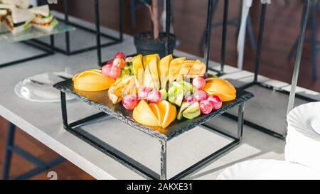 Close-up of fresh tropical fruits. Sliced banana, kiwi, orange and grape are on the plate. Concept of healthy eating and catering service Stock Photo