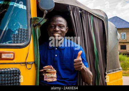 young african man driving a rickshaw taxi counting his money smiling giving a thumbs up Stock Photo