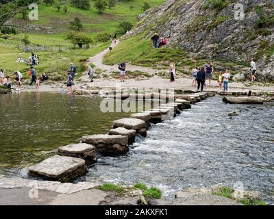 Tourists enjoy the great outdoors by the famous Stepping Stones across the River Dove below the flanks of Thorpe Cloud in Dovedale, Derbyshire. Stock Photo