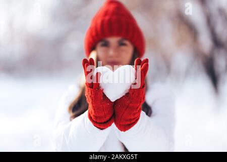 Woman in red gloves and hat holding heart shape from snow Stock Photo