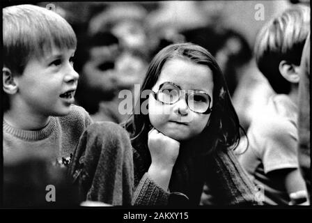 Very real intentful little girl watching others during assembly at school for first grade students in black and white from film Stock Photo