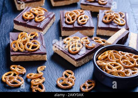 close-up of No-Bake Chocolate Peanut Butter Bars topped with pretzel crackers on a slate tray on a wooden table, view from above Stock Photo