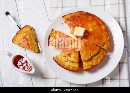 Homemade sliced Buttermilk Cornbread topped with melted butter served on a plate with maple syrup in a gravy boat on a white wooden table Stock Photo
