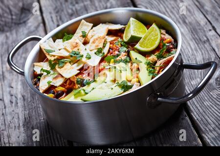 close-up of mexican shredded Chicken Taco Soup with black bean, corn kernels, topped with tortilla strips, avocado slices and lime in a metal pot on a Stock Photo
