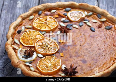 Sweet potato pie decorated with orange chips, pumpkin seeds and anise stars on a rustic wooden table, horizontal view from above, close-up Stock Photo