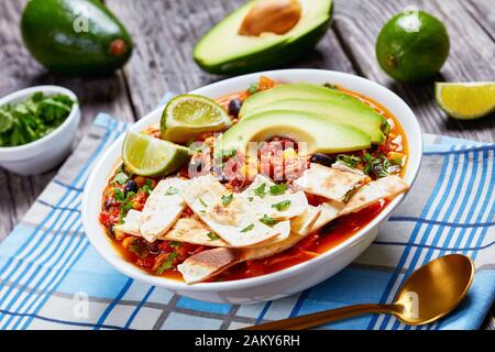 close-up of mexican shredded Chicken Taco Soup with black bean, corn kernels, topped with tortilla strips, avocado slices and lime in white bowl on a Stock Photo