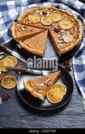 sliced Sweet potato pie decorated with orange chips, pumpkin seeds and anise stars on a black plate on a wooden table, vertical view from above, close Stock Photo