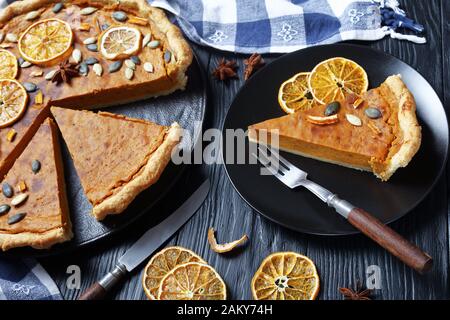 sliced Sweet potato pie decorated with orange chips, pumpkin seeds and anise stars on a black plate on a wooden table, horizontal view Stock Photo