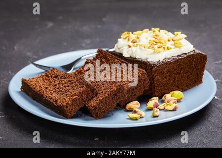 Dark Molasses Gingerbread Cake with fresh whipped cream on top and finely chopped pistachios, horizontal view from above, close-up Stock Photo
