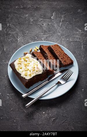 Dark Molasses Gingerbread Cake with fresh whipped cream on top and finely chopped pistachios served on a plate on a concrete table, vertical view from Stock Photo
