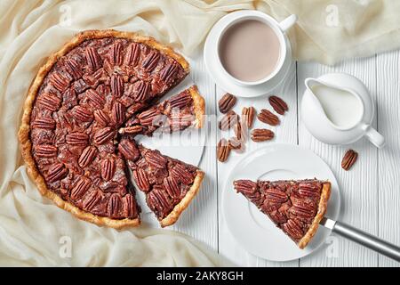 pecan pie sliced on a white platter served with hot chocolate milk, horizontal view from above, close-up, flatlay Stock Photo